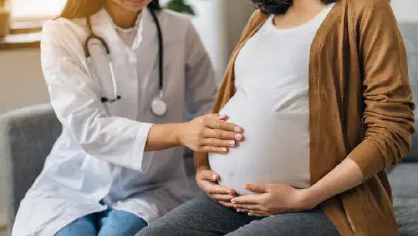 Doctor consulting with a pregnant woman, placing hand gently on her stomach